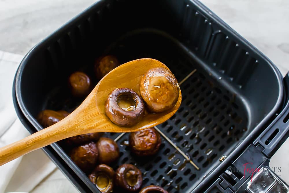 cooked mushroom caps on a wooden spoon above an air fryer basket.