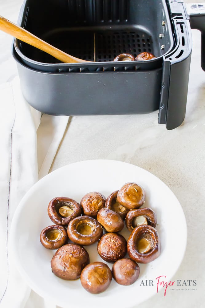 cooked mushroom caps on a white plate, next to an air fryer basket.