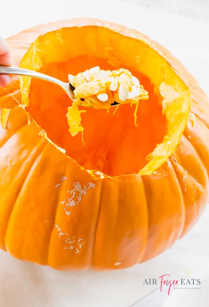 large orange pumpkin pictured with hole cut in top and spoon on top with pulp and seeds