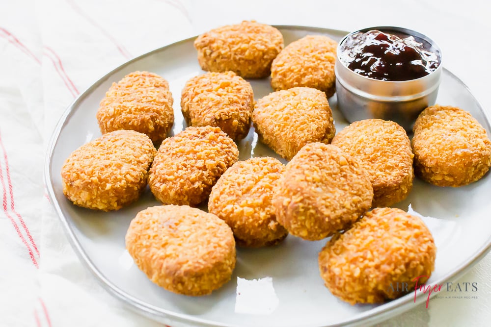 chicken nuggets on a white plate with a small tin of bbq sauce. A white and red striped napkin under the plate.
