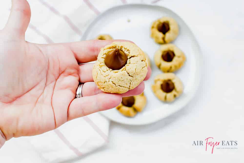 A hand holding a peanut butter blossom over a plate of more cookies