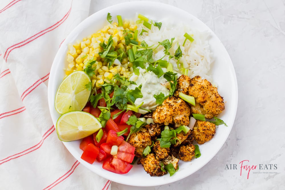 A cauliflower taco bowl with corn, tomatoes, lime crema, white rice, and cilantro