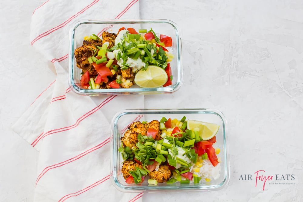 Glass meal prepped taco bowls with cauliflower, rice, tomatoes, corn, green onions, and cilantro