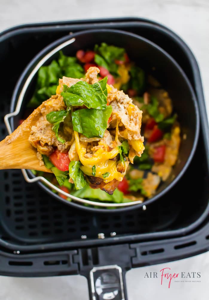 closeup image of Taco pie being served on a wooden spoon over a black air fryer basket with a pot inside.