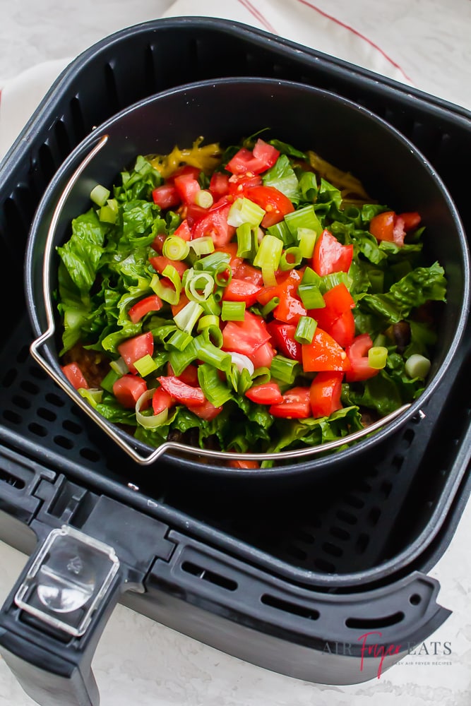 Air fryer taco pie. Finished dish in the air fryer, topped with lettuce, tomato, and green onion.