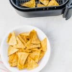 plate of tortilla chips next to an air fryer basket with tortilla chips in it