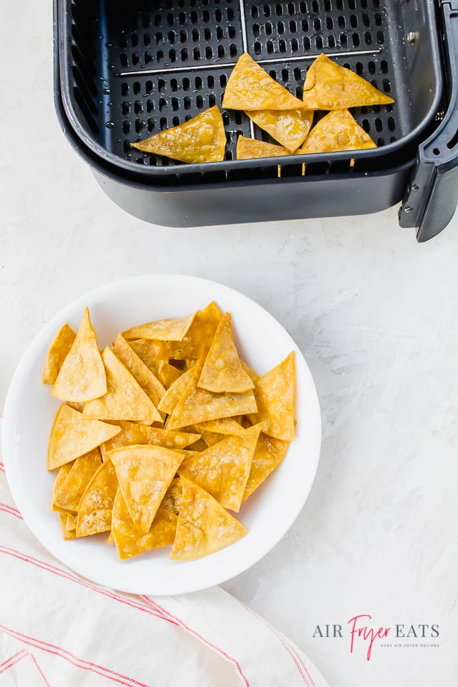 a white plate of tortilla chips next to a air fryer basket of tortilla chips