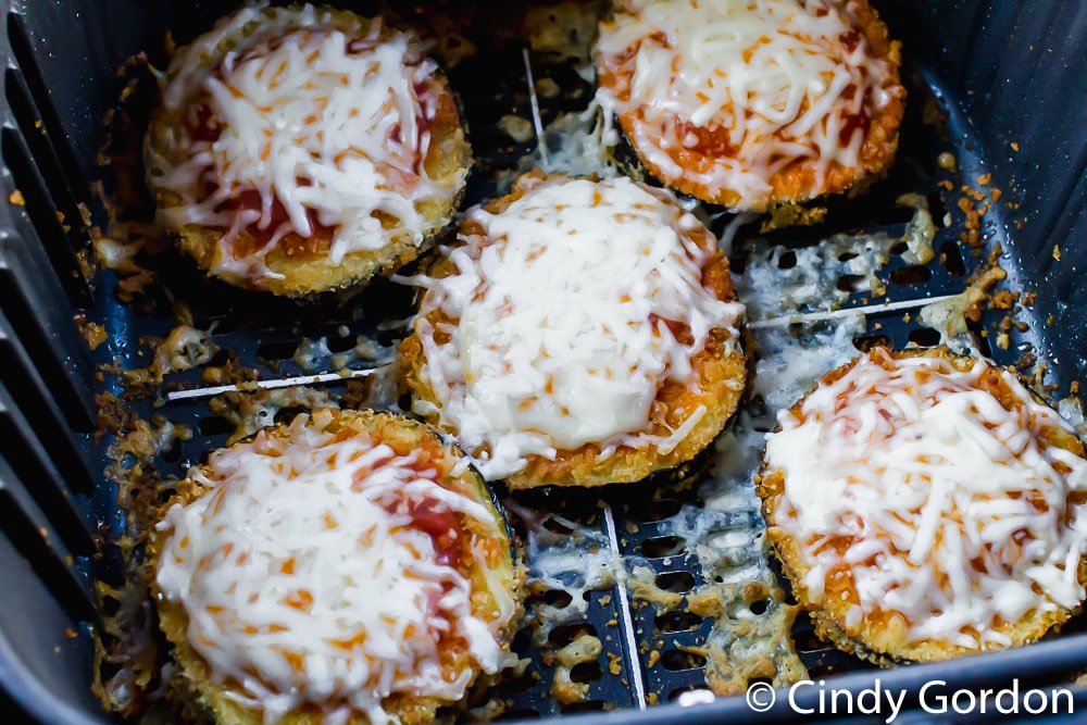 eggplant parmesan slices topped with sauce and cheese in an air fryer basket. 