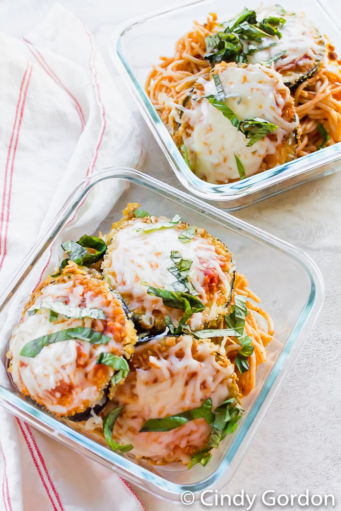 two square glass dishes filled with spaghetti and eggplant parmesan slices.