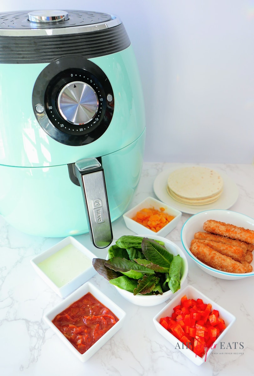 ingredients needed to make easy air fryer fish tacos next to a teal dash air fryer