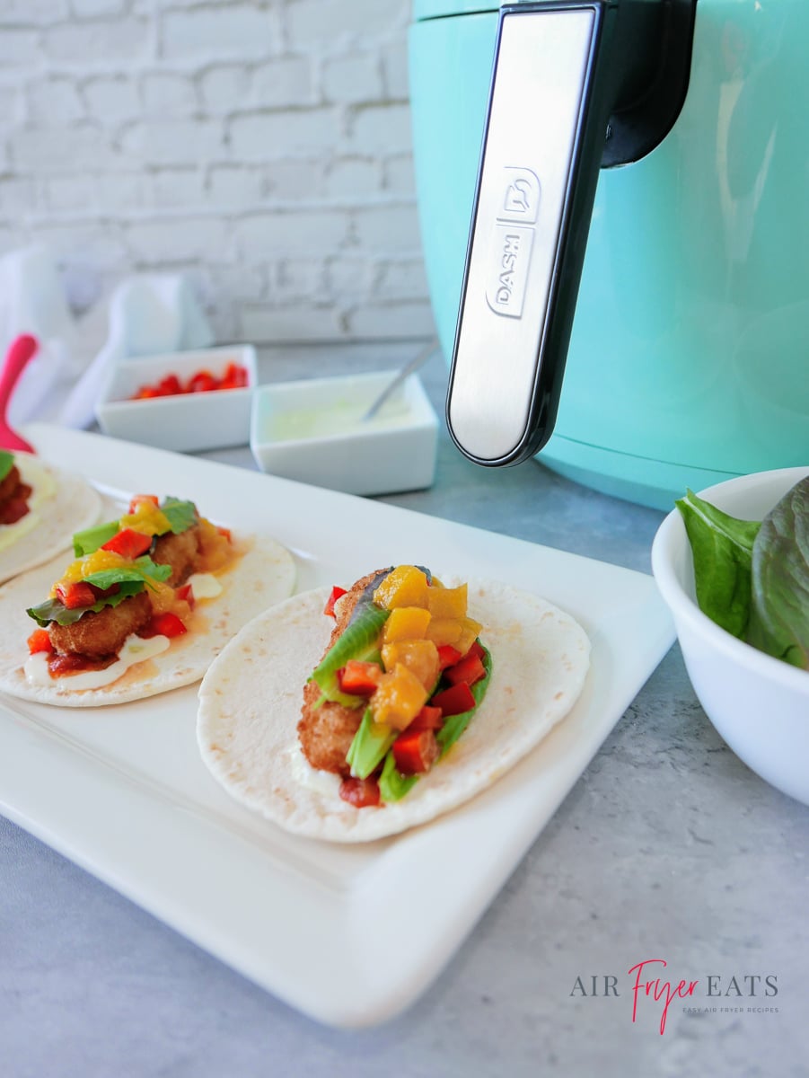 mini air fryer fish tacos with peaches on a white platter next to a blue dash air fryer.