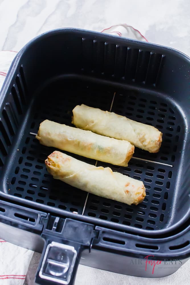 A square air fryer basket with three eggrolls in it.