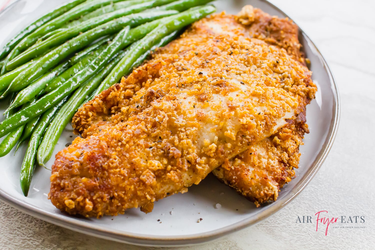Tilapia with a breadcrumb crust on a gray round plate with green beans