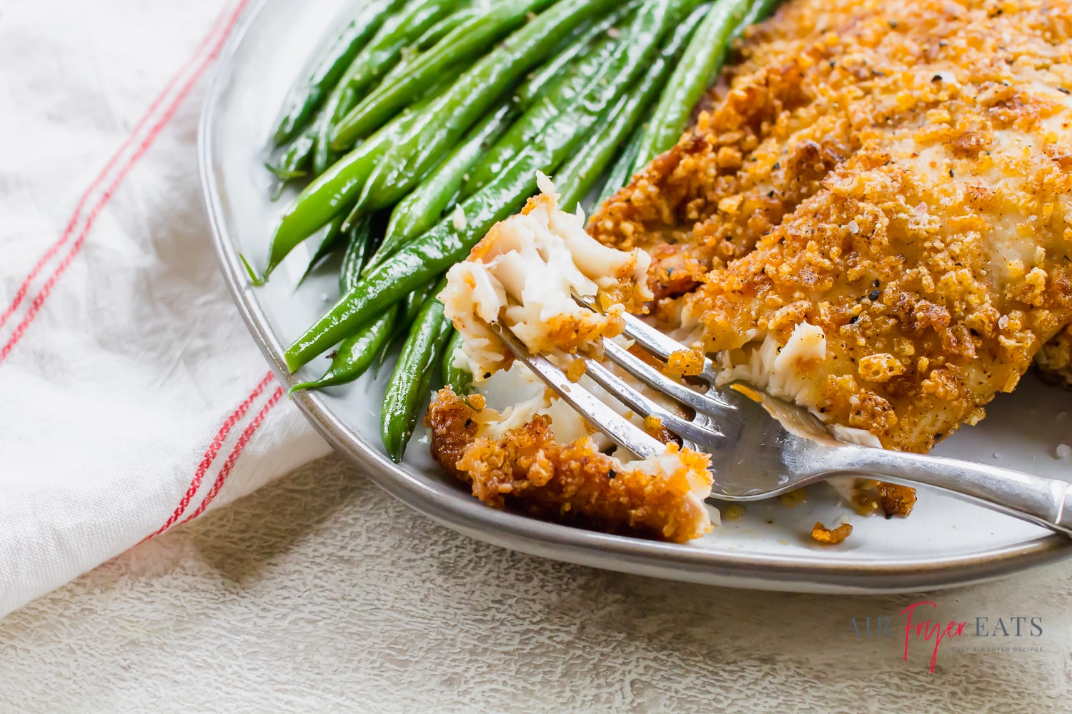 Close-up shot of flaky white fish on a fork with a breadcrumb crust next to green beans