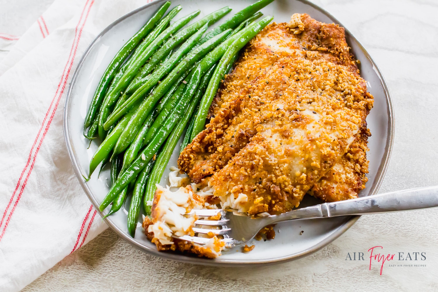 Flaky air fryer tilapia with green beans on a round gray plate with a fork