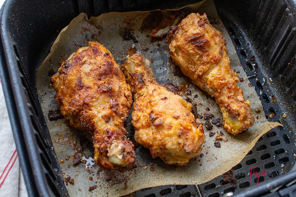 3 fried chicken drumsticks on parchment paper in an air fryer basket