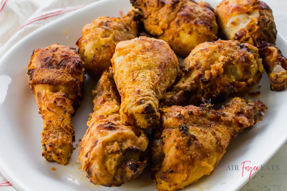 8 fried chicken legs on a serving platter with a red and white kitchen towel