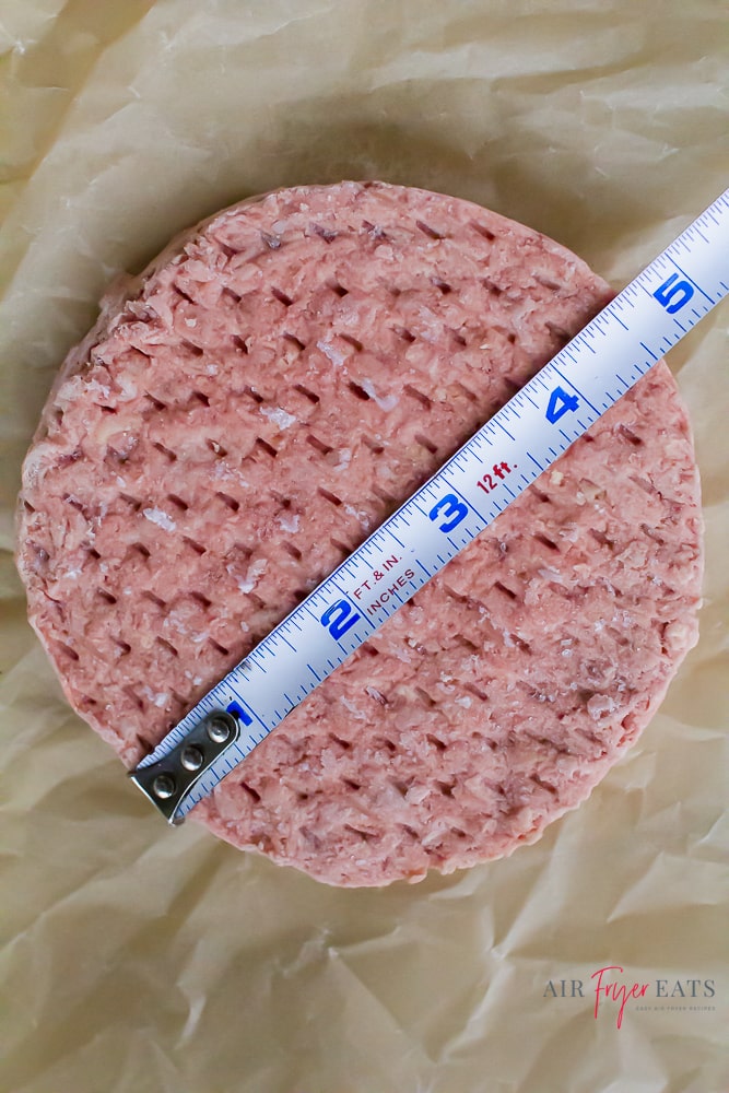 raw frozen burger with tape measure on top. Measures to 4.5 inches