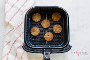 square air fryer basket with 6 cooked, round sausage patties