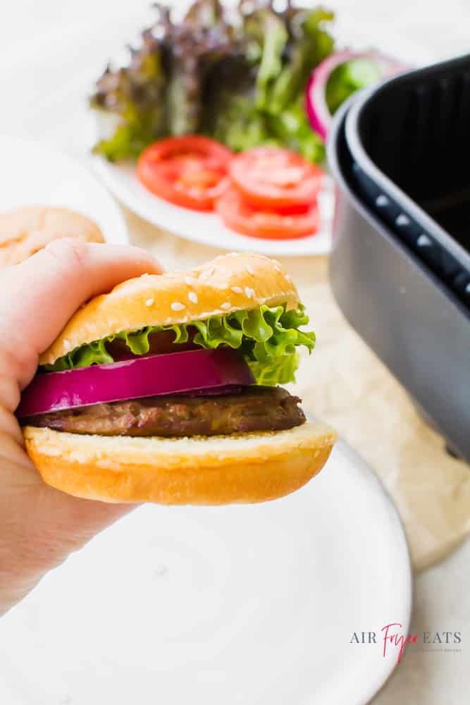 Someone holding a turkey burger on a sesame seed bun with lettuce, tomato, and red onion