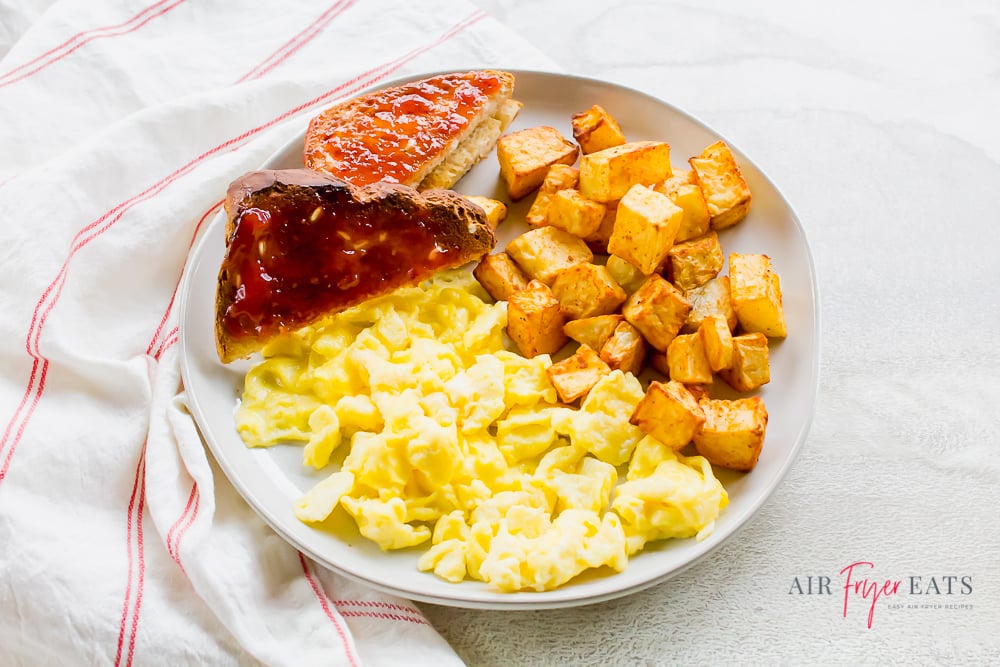 Breakfast plate including scrambled eggs, toast with jam, and breakfast potatoes
