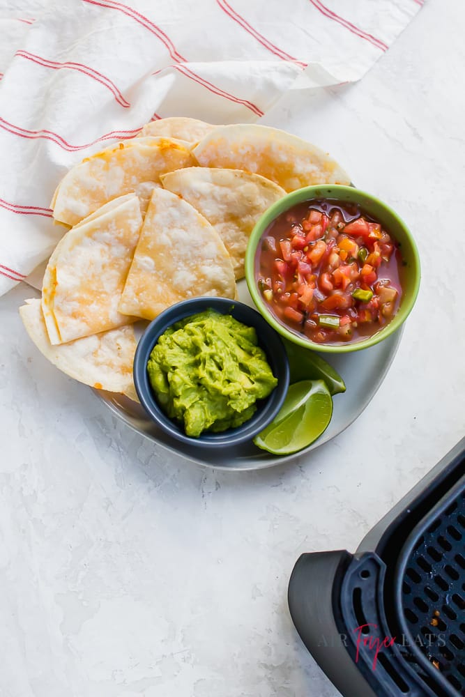 a plate of quesadillas with salsa and guacamole next to an air fryer basket.