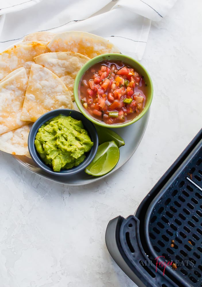 a plate of quesadillas with salsa and guacamole next to an air fryer basket.