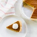 air fryer pumpkin pie slice on a white plate with whipped cream and the rest of the pie on the top right