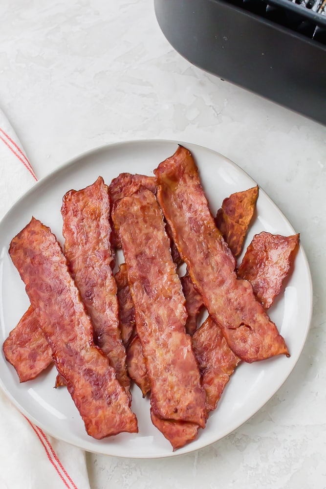 a plate of cooked turkey bacon next to an air fryer.