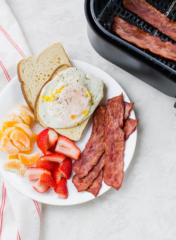 a plate of eggs, bacon, toast and fruit