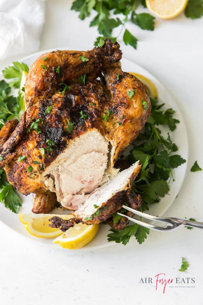 A whole rotisserie chicken with parsley and lemon slices carved through the breast