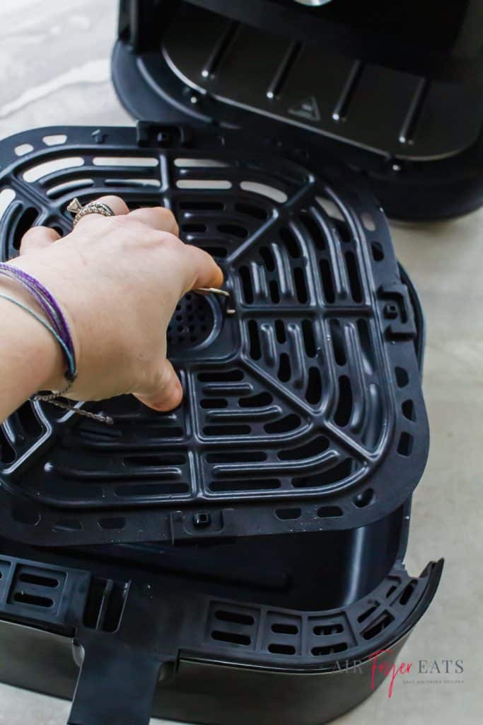instant vortex black unit and basket. hand holding the crisper plate over the empty basket