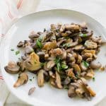 a plate of cooked mushrooms topped with herbs