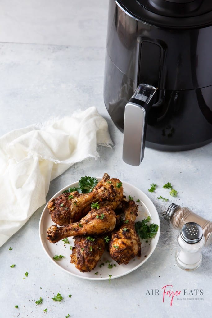 a plate of chicken legs next to an air fryer basket and a white towel. 