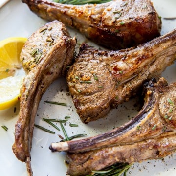 4 cooked lamb chops on a plate garnished with lemon and rosemary
