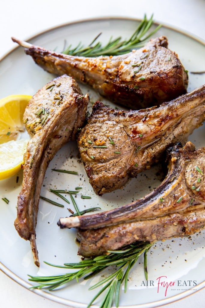 4 cooked lamb chops on a plate garnished with lemon and rosemary