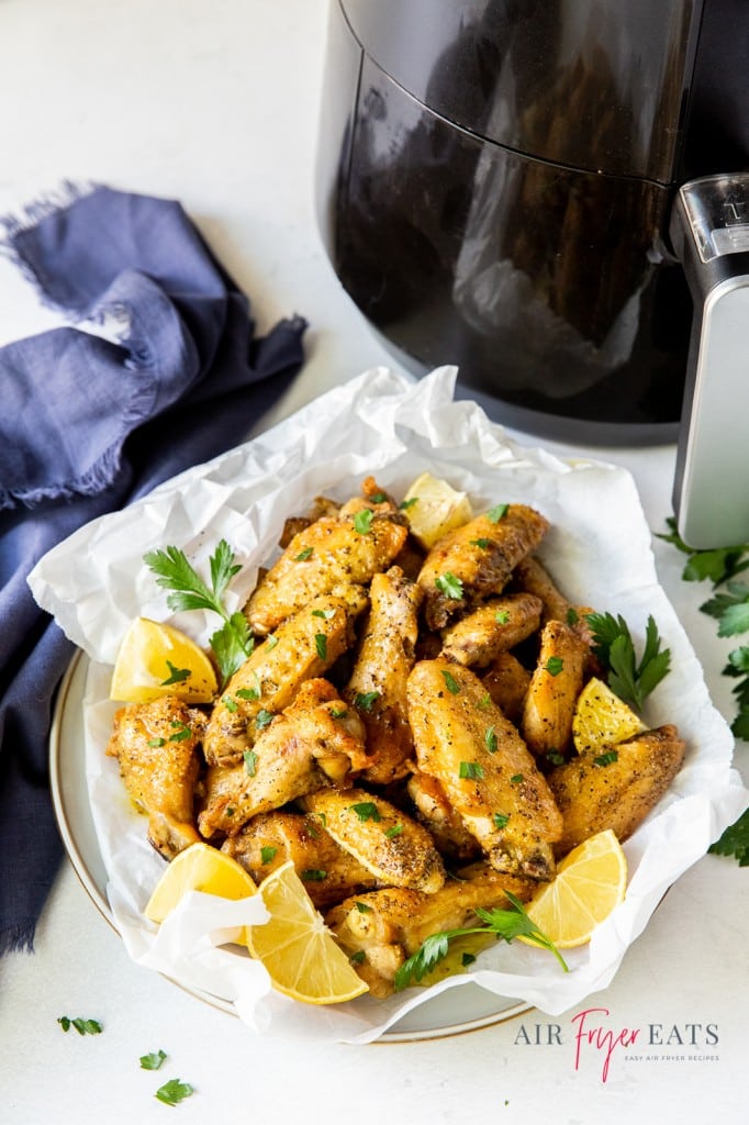 a plate of air fryer chicken wings with lemon pepper sauce, next to an air fryer