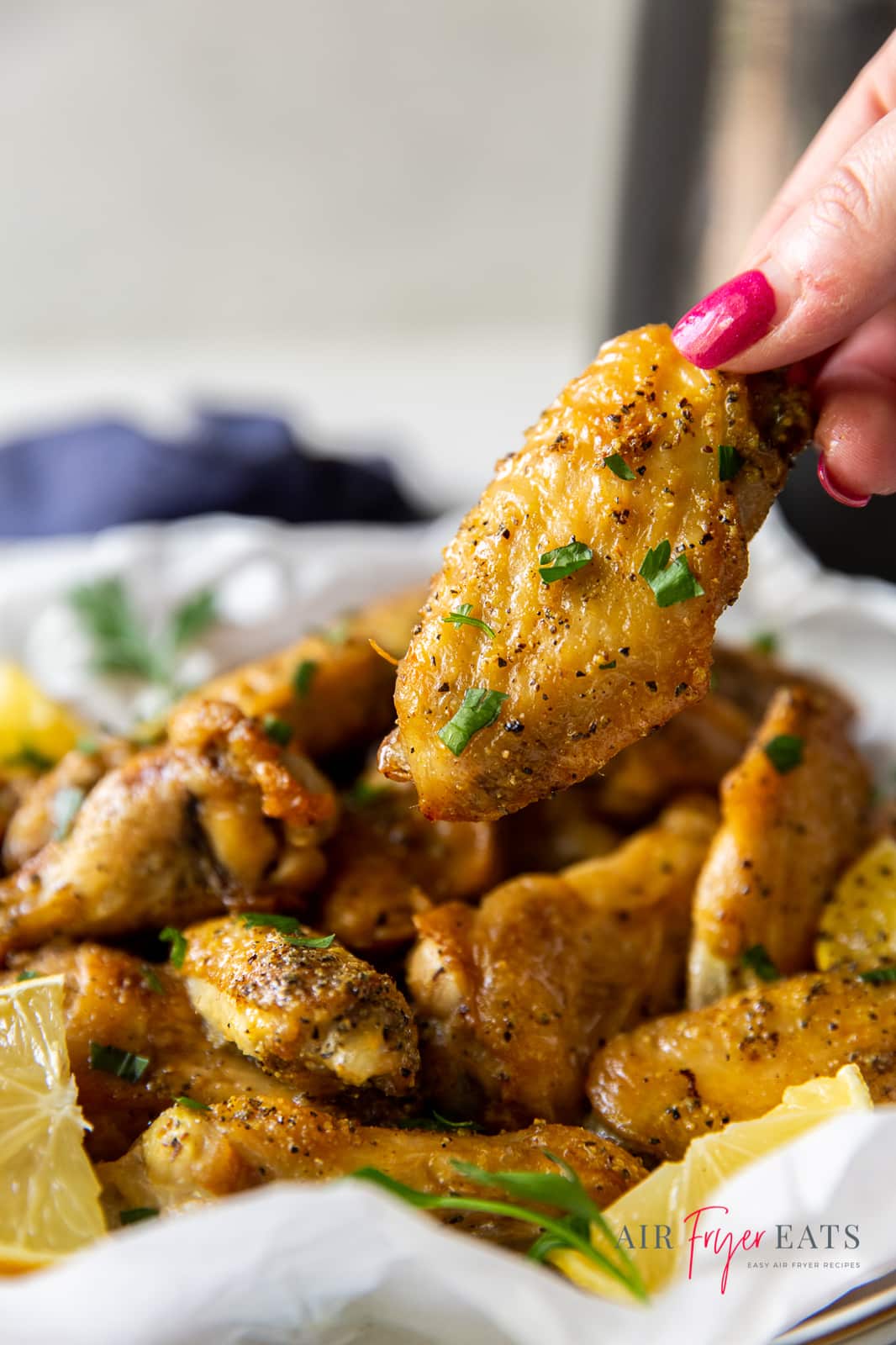 a plate of lemon pepper chicken wings. a hand is picking up a flat wing.