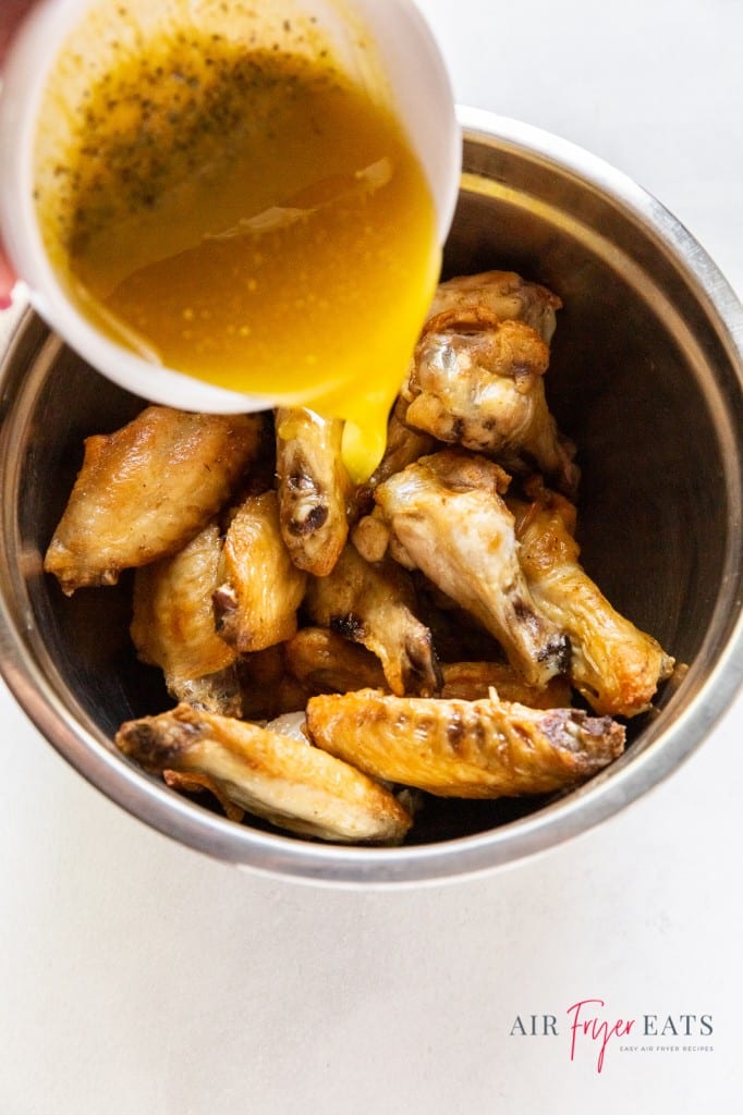 chicken wings in a bowl with lemon pepper sauce being poured on. 
