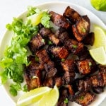 a white plate of pork belly pieces, lettuce, and lemon wedges