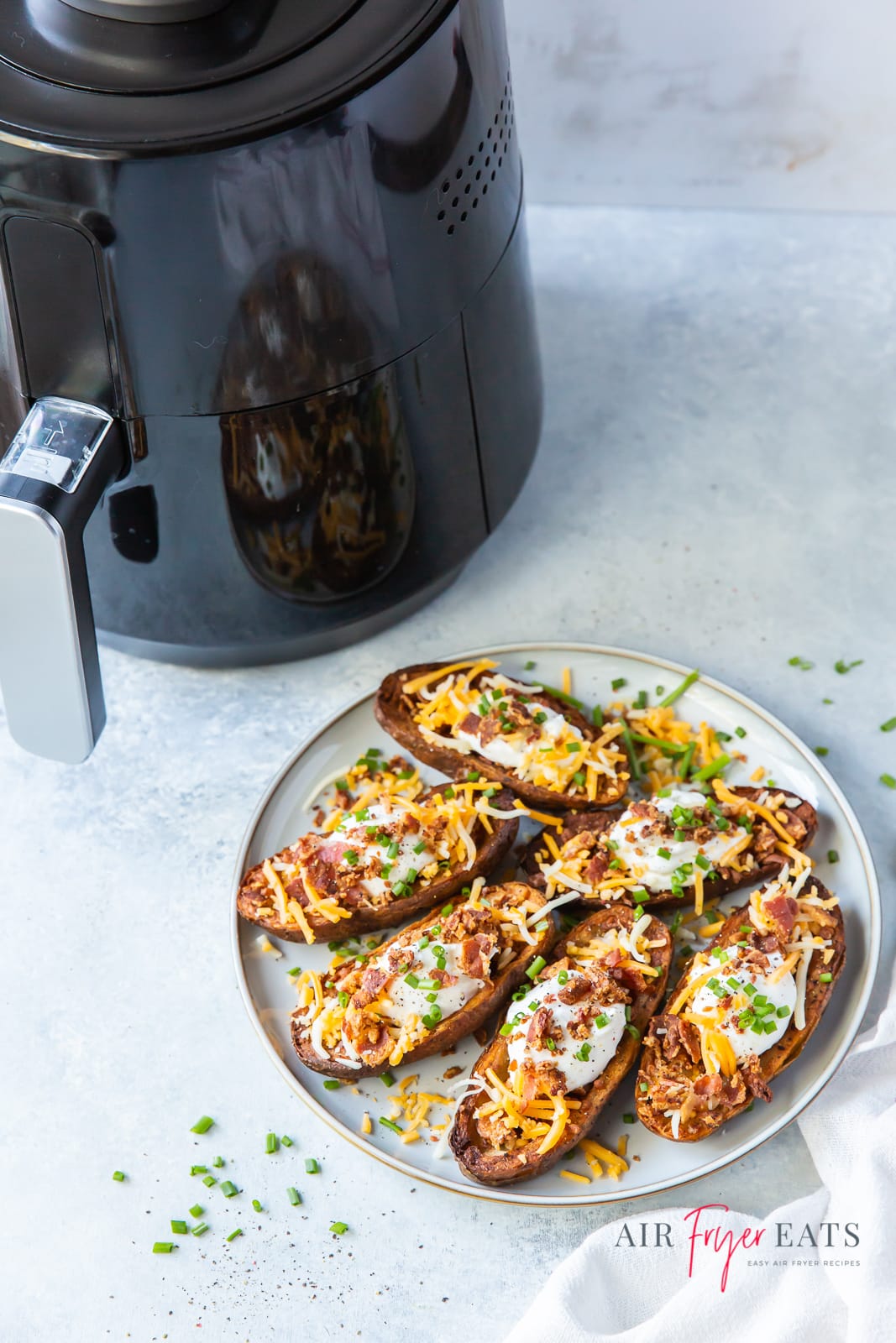 a plate of loaded potato skins next to a black air fryer.