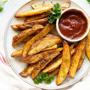a plate of seasoned, cooked potato wedges with a side cup of ketchup.