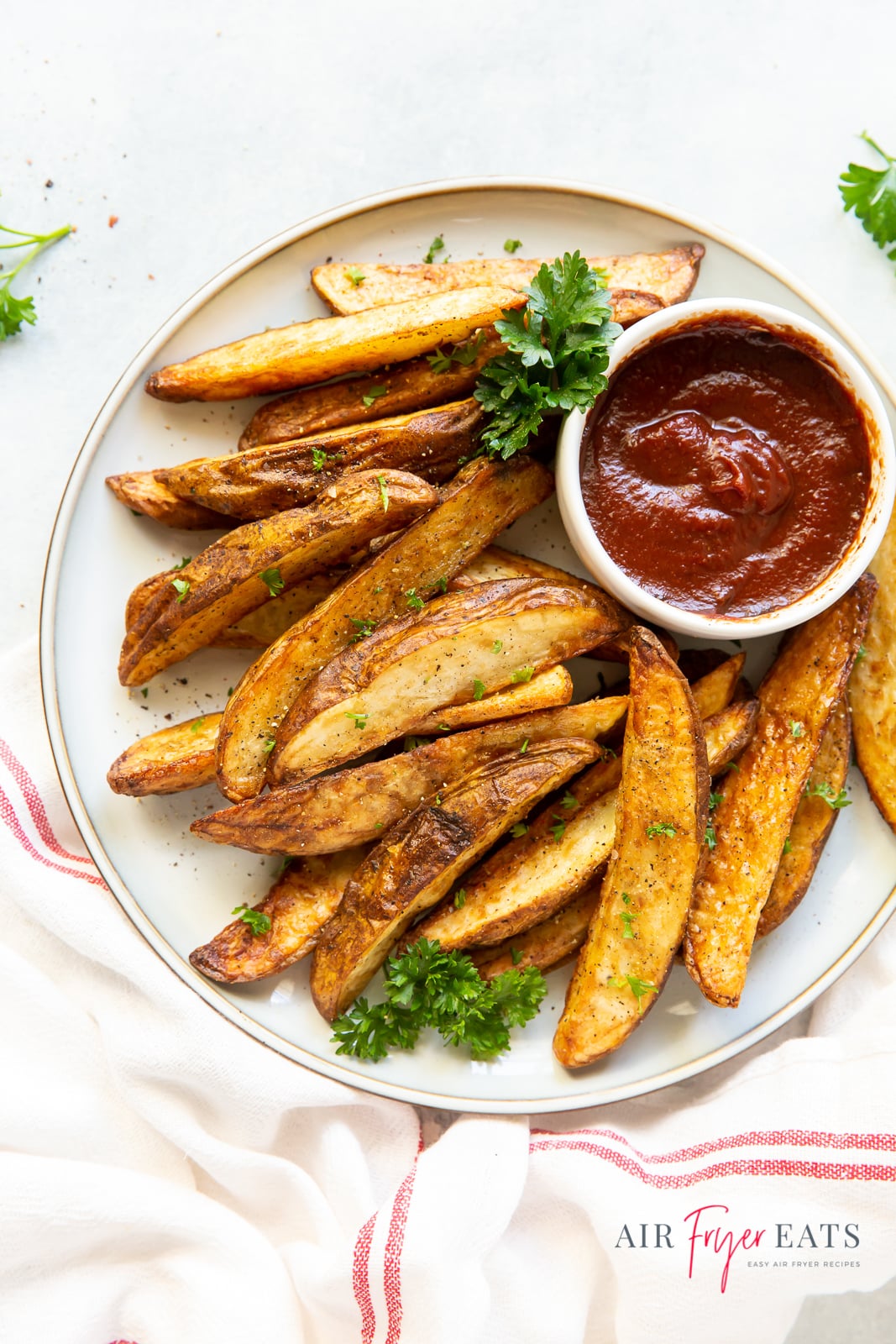 a plate of seasoned, cooked potato wedges with a side cup of ketchup.