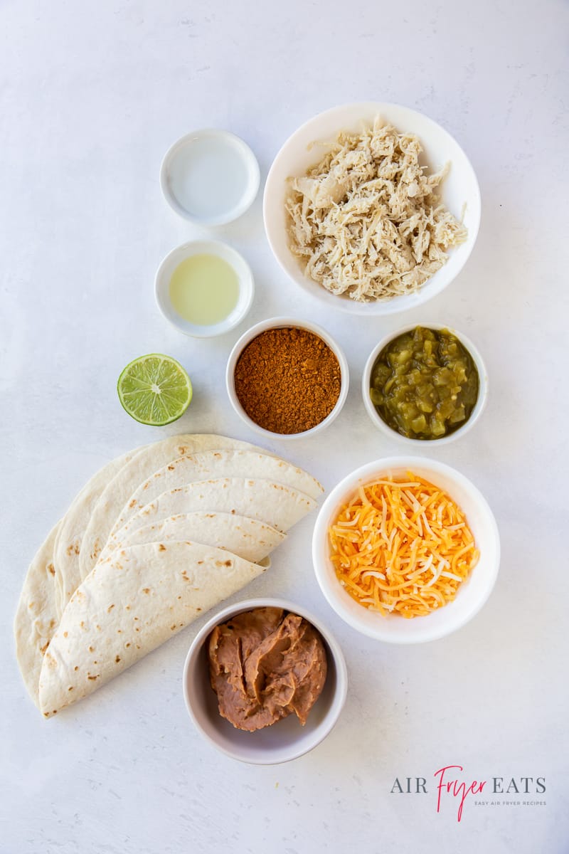 top down view of all of the ingredients needed to make chicken chimichangas in the air fryer. Including tortillas, cheese, chicken, seasonings, and lime.