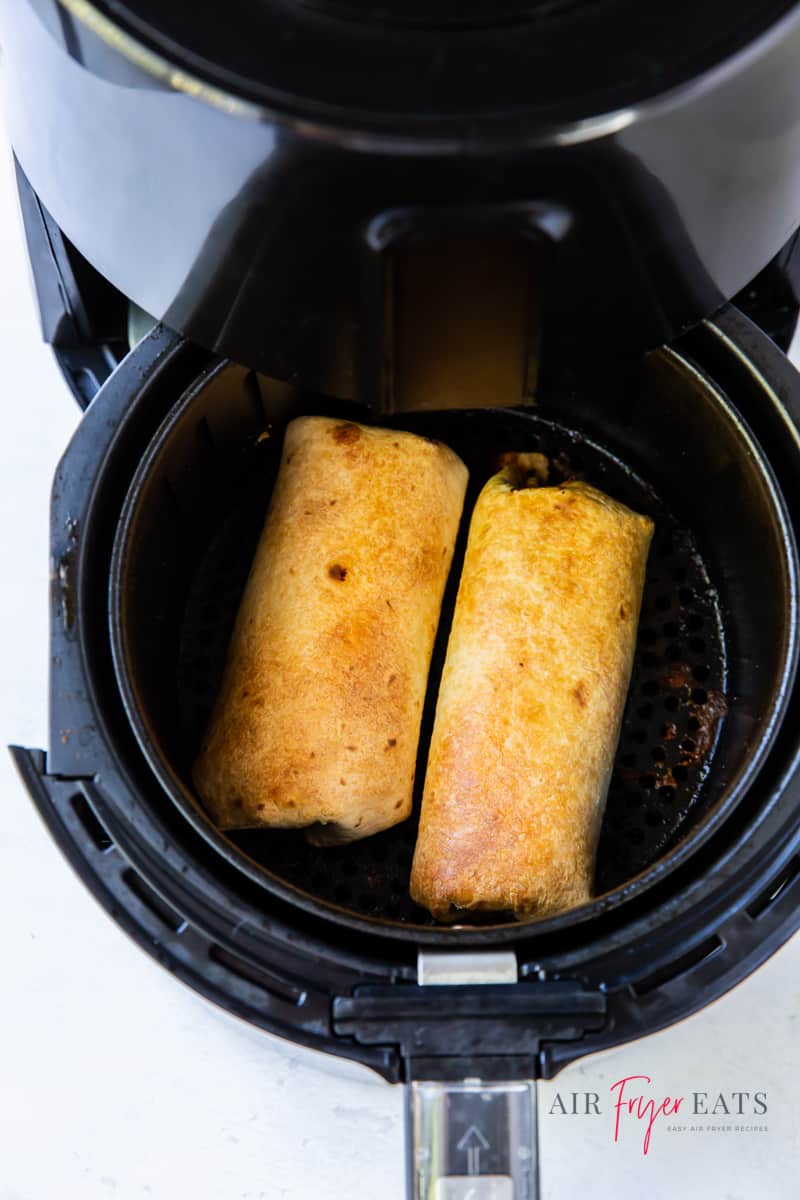 a round air fryer basket with two chimichangas inside.