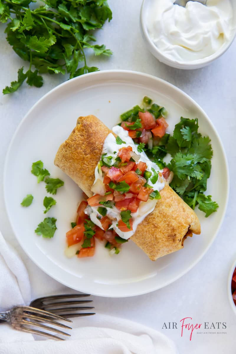 a chimichanga on a white plate topped with sour cream and salsa