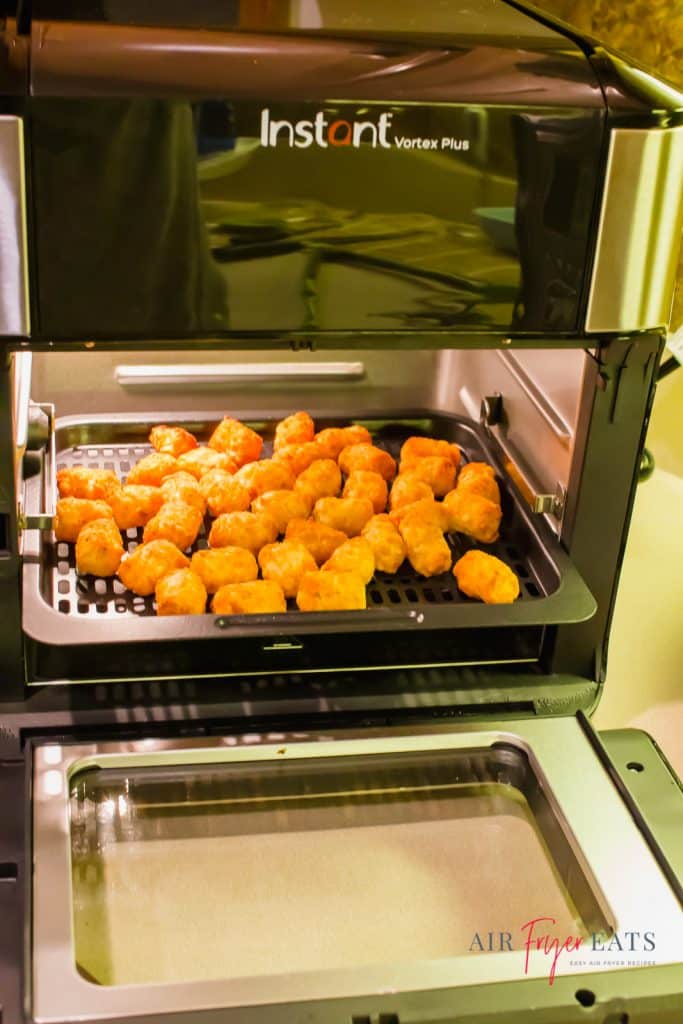 picture of instant vortex plus air fryer oven with door open and tater tots inside