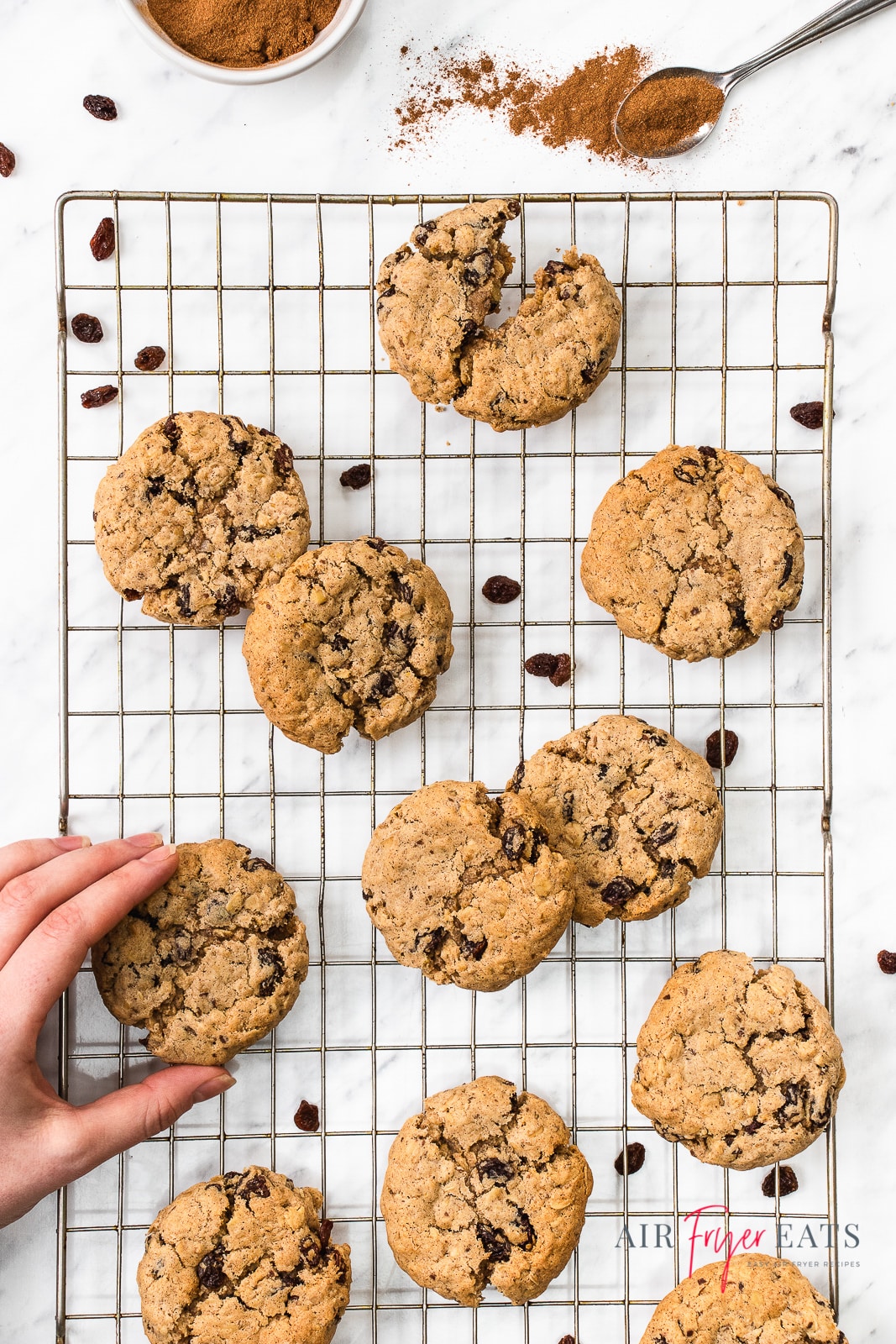 A cooling rack filled with oatmeal raisin cookies with a hand grabbing one.