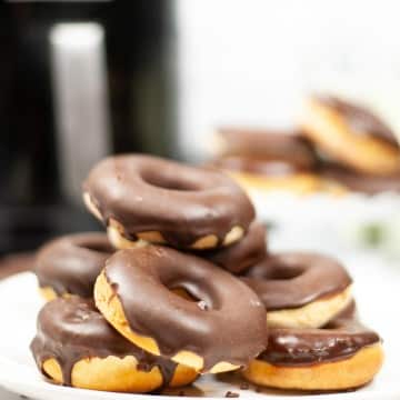 a white plate toped with a stack of 6 donuts that are iced with chocolate