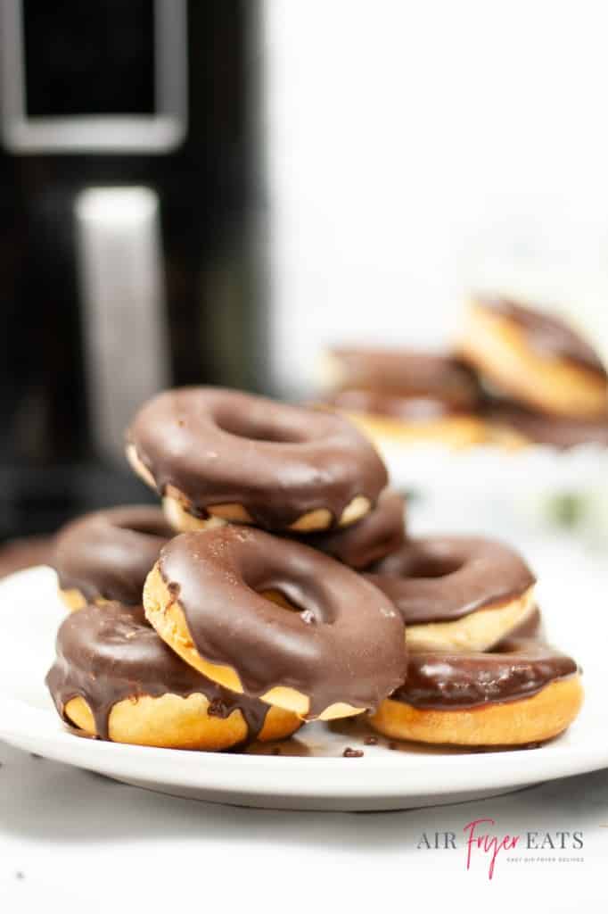 a white plate toped with a stack of 6 donuts that are iced with chocolate